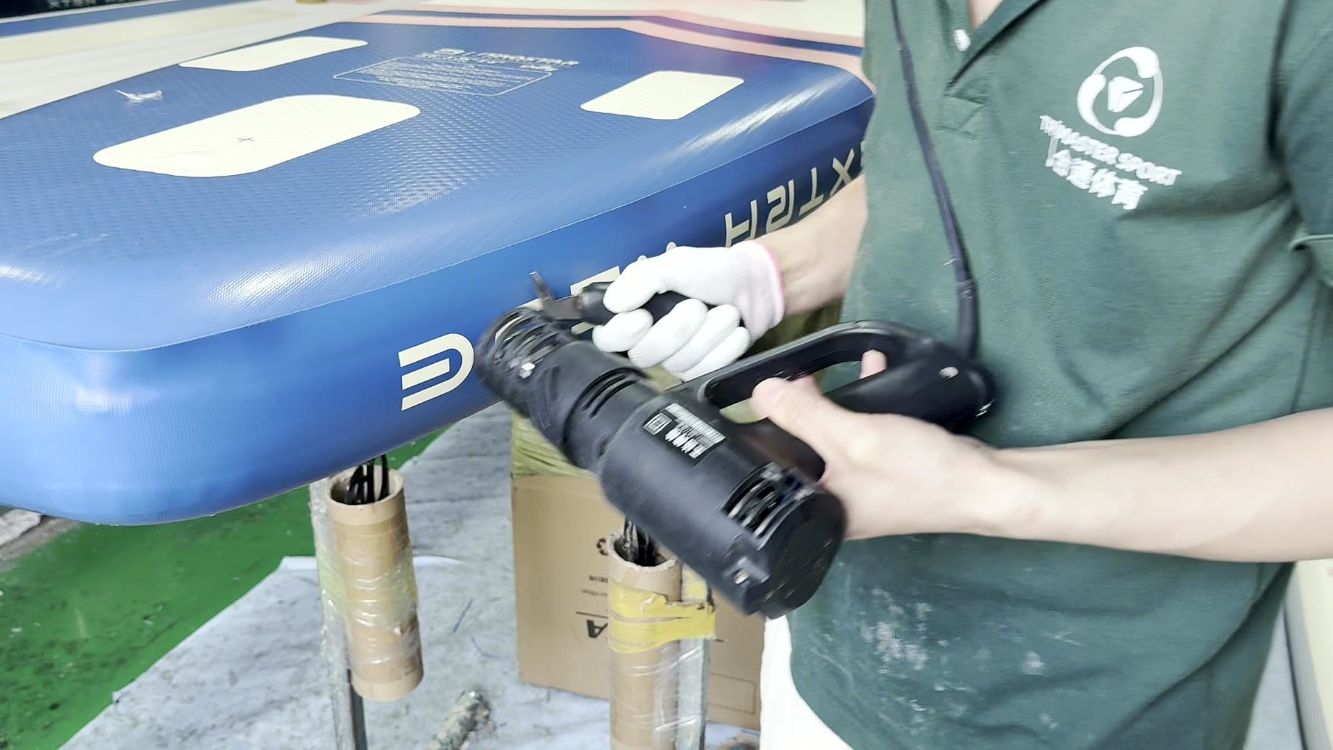 Gloved hand running a heat gun along the outer rail of a blue board.