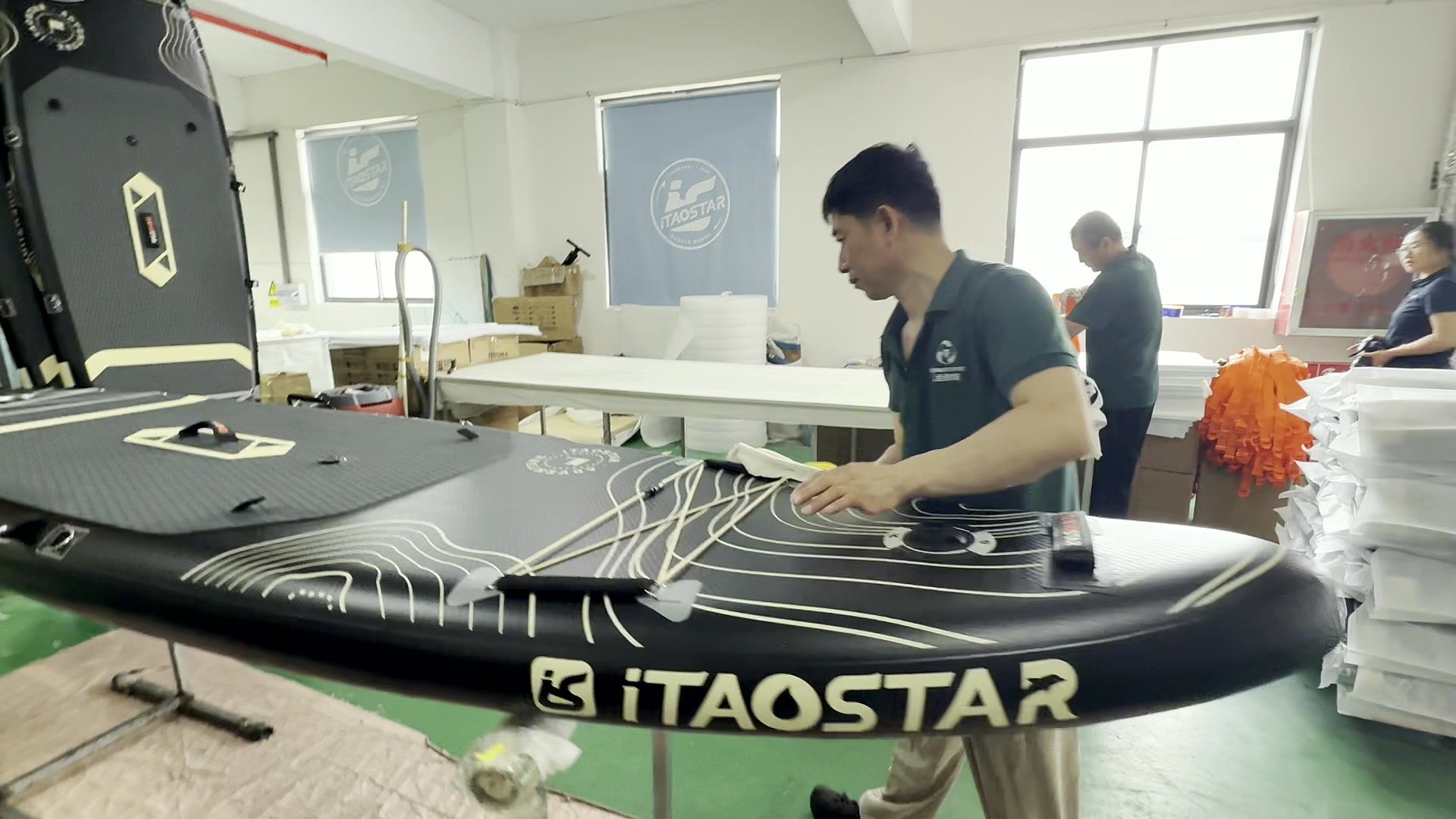 Worker cleaning a finished paddle board with a cloth.
