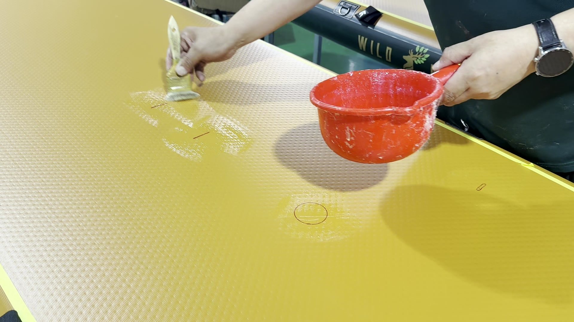 Hand brushing adhesive around an accessory mount beside a glue bowl.